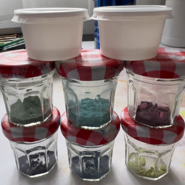 Photo of small jars and condiment cups, holding broken bits of pastels and pastel dust.